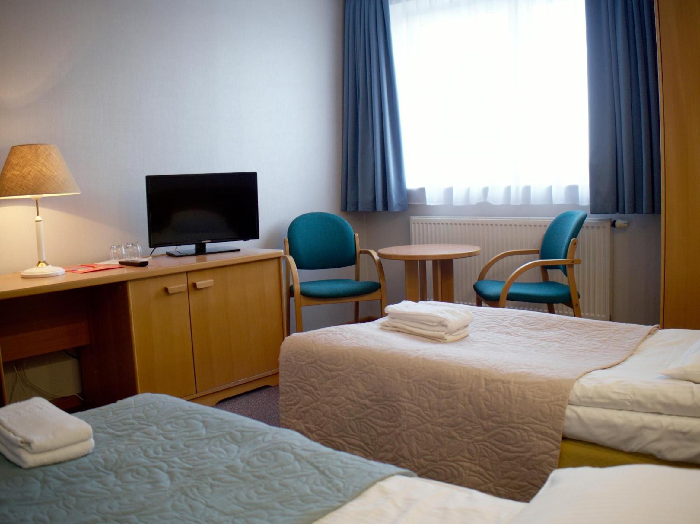 Ett hotellrum med en säng, ett skrivbord med en tv, en stol och ett litet bord.