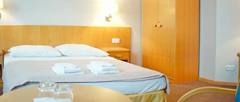 A hotel room with a bed, bedside tables, a wardrobe, and a round table with a glass.