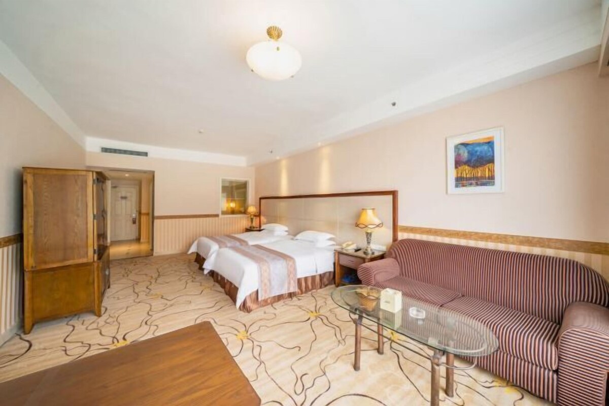 Una habitación de hotel con una cama, un sofá, una mesa de vidrio y un armario de madera.