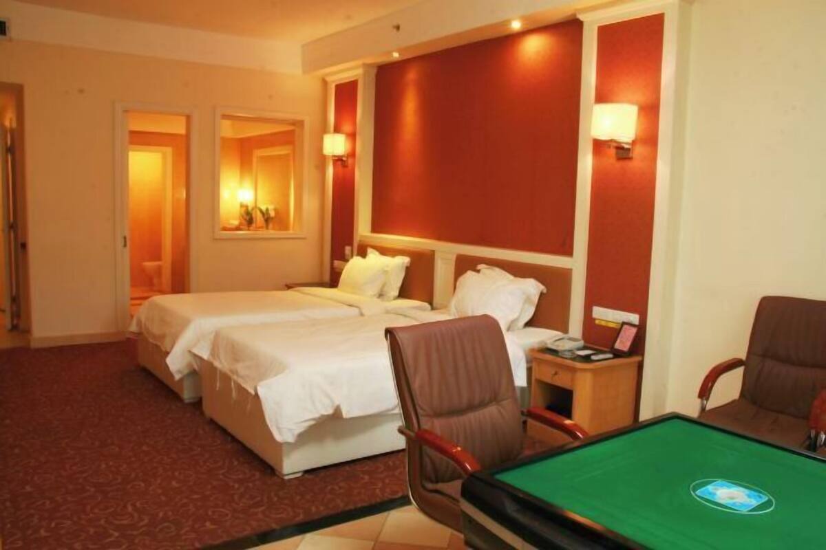 A hotel room with two beds, a pool table, and a desk with a lamp.