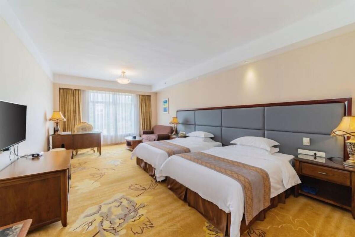 Habitación de hotel con dos camas, televisión, escritorio y ventana con cortinas.