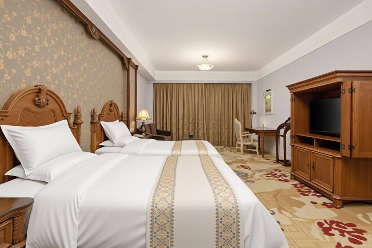 A hotel room with two beds, a desk, a television, and a large window with curtains.