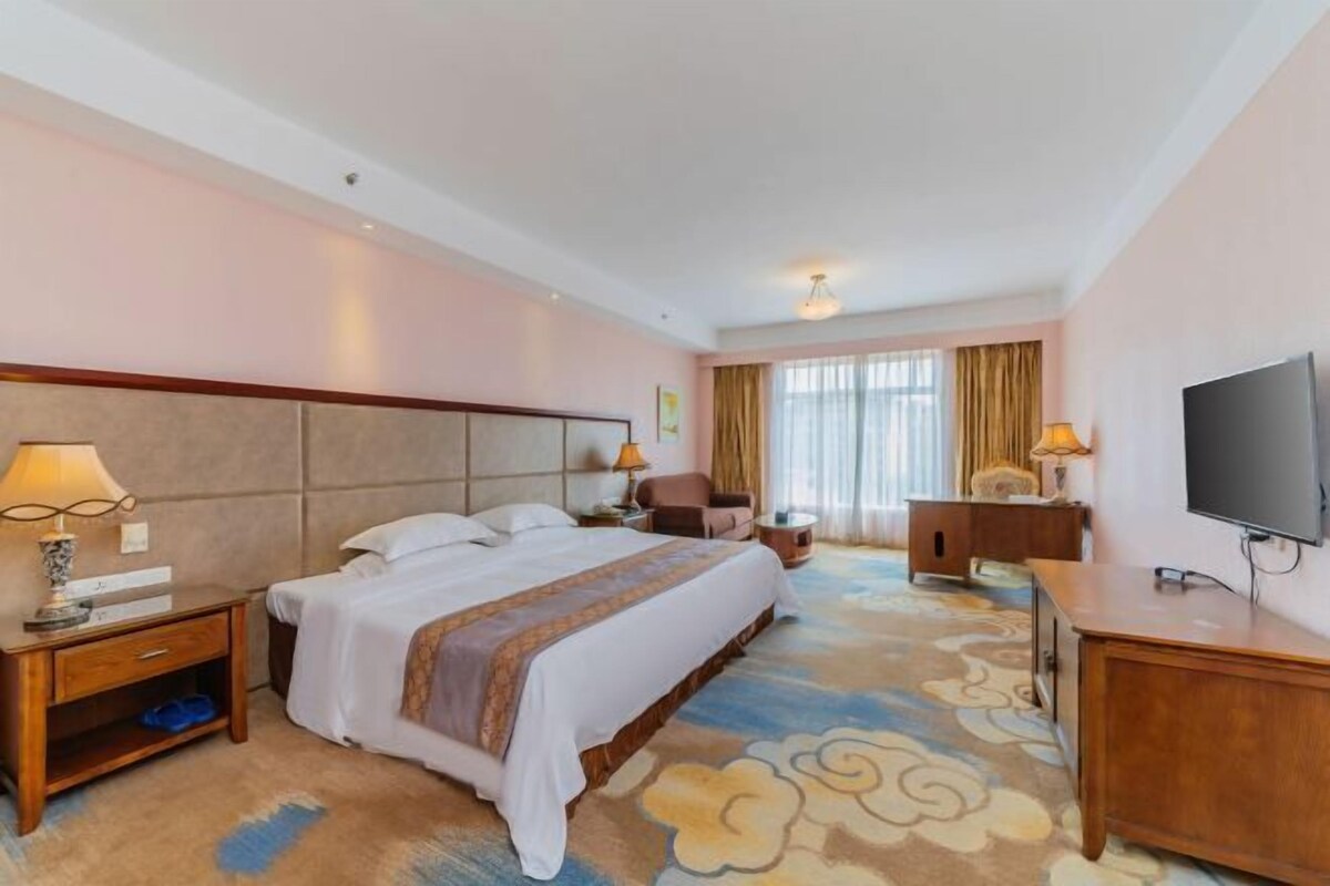 Una habitación de hotel con cama, mesitas de noche, televisor, escritorio y una silla.