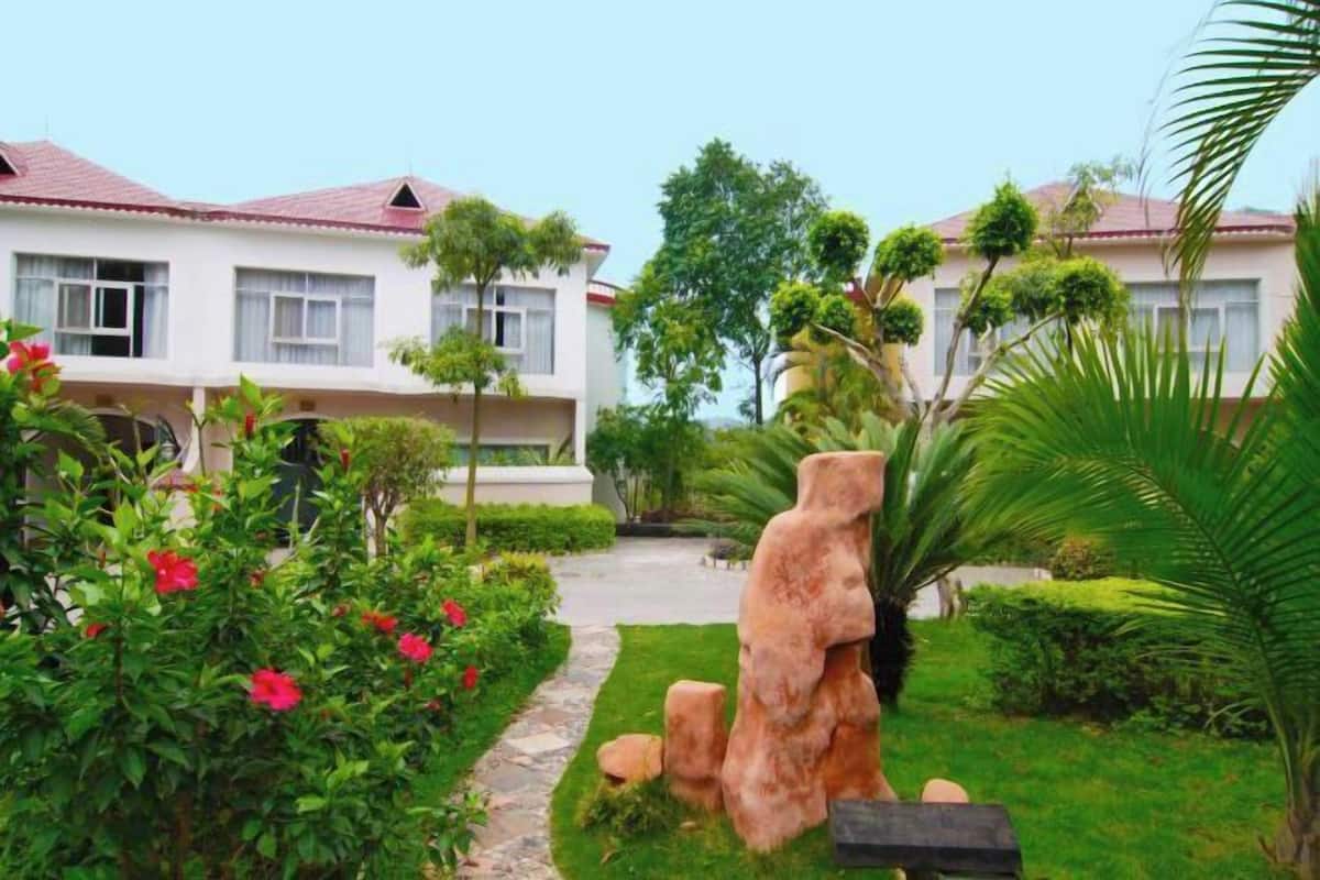 A hotel with a garden pathway, a large rock sculpture, and neatly trimmed hedges.