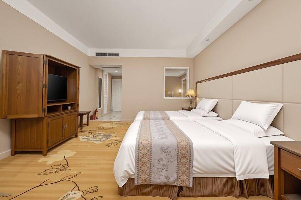 A hotel room with a bed, a wooden wardrobe, a television, a bedside table, and a mirror.