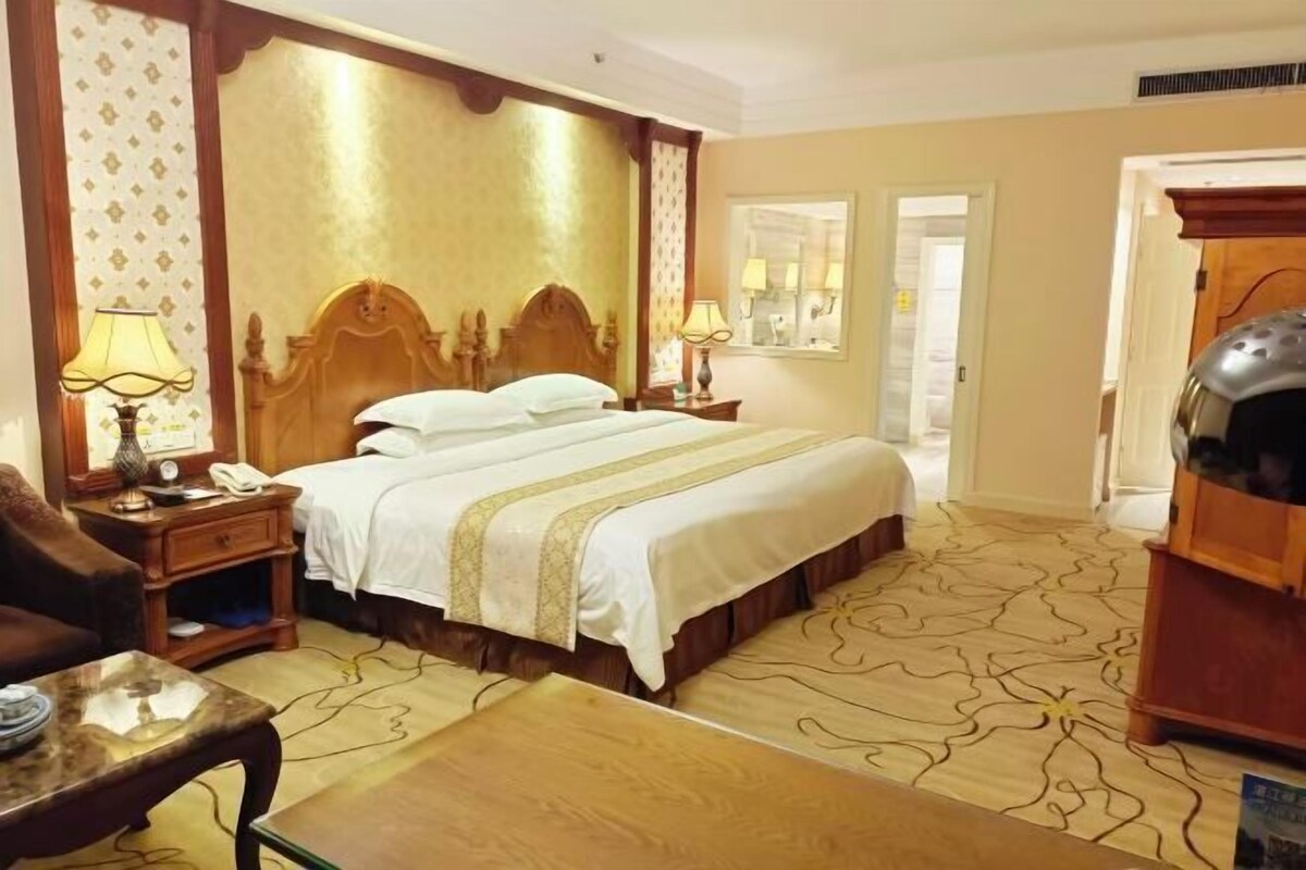 Una habitación de hotel con una cama grande, una mesita de noche de madera, un escritorio y una silla.