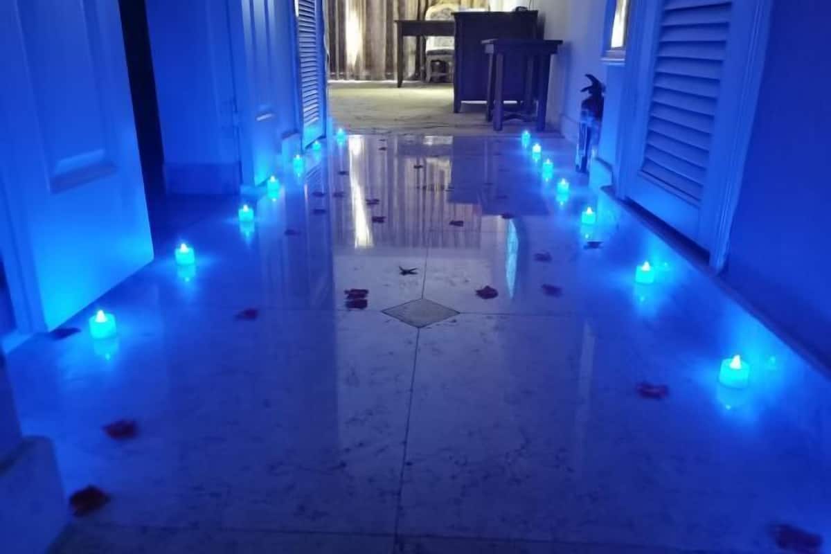 A hallway with a reflective floor, blue lighting, and scattered candles.