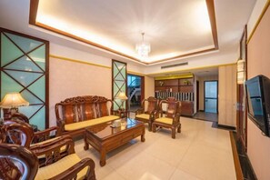 Un salón amplio con sofá, sillones y una mesa de centro. Hay un televisor a la derecha y una escalera que sube a otro nivel.