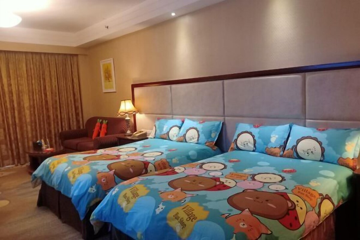 Habitación de hotel con dos camas, un sillón de cuero marrón, una mesita de noche con lámpara y una ventana con cortinas.
