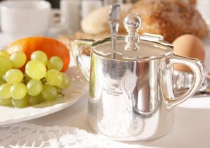A silver teapot with a lid on a table, accompanied by a plate of green grapes and an orange. - Hotel Stadt Hannover (Goettingen)
