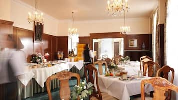 Ein stilvolles Esszimmer mit mehreren Tischen, Kristalllüstern und Holzvertäfelung.