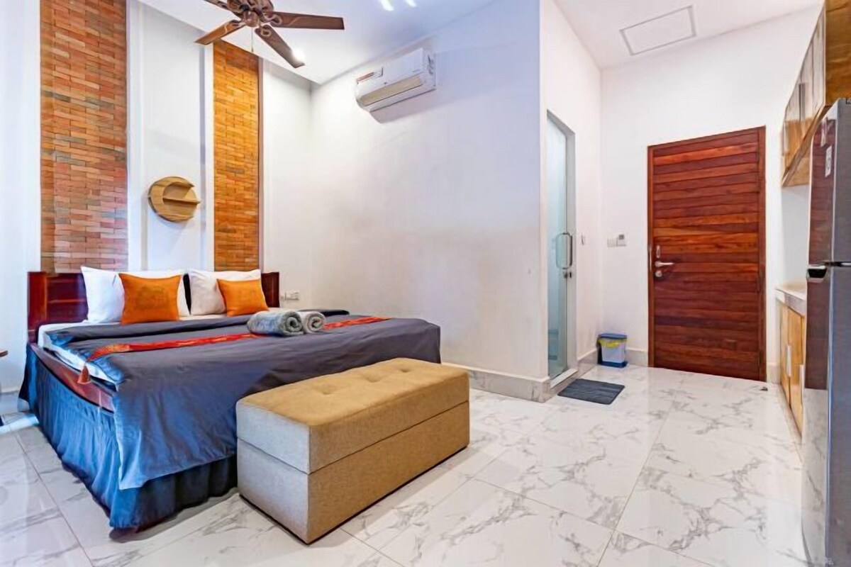 Une chambre à coucher avec un lit, un banc, un ventilateur de plafond et une porte.