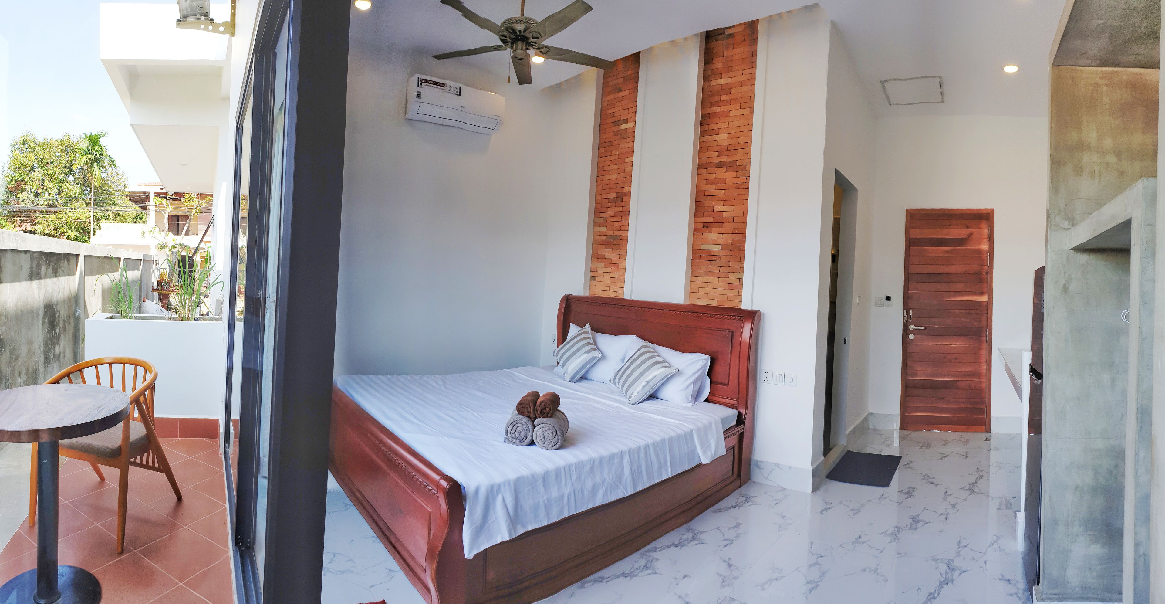 Ein Schlafzimmer mit einem hölzernen Bett, einem Deckenventilator und Blick auf den Balkon.