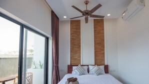 A hotel room with a large bed, a ceiling fan, a brick accent wall, and a sliding glass door to a balcony.