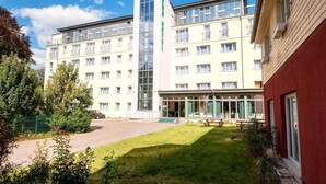 A hotel with a central tower labeled 'HOTEL,' multiple windows, a grassy courtyard, and a red building to the right. - Alpha (Bad Langensalza)