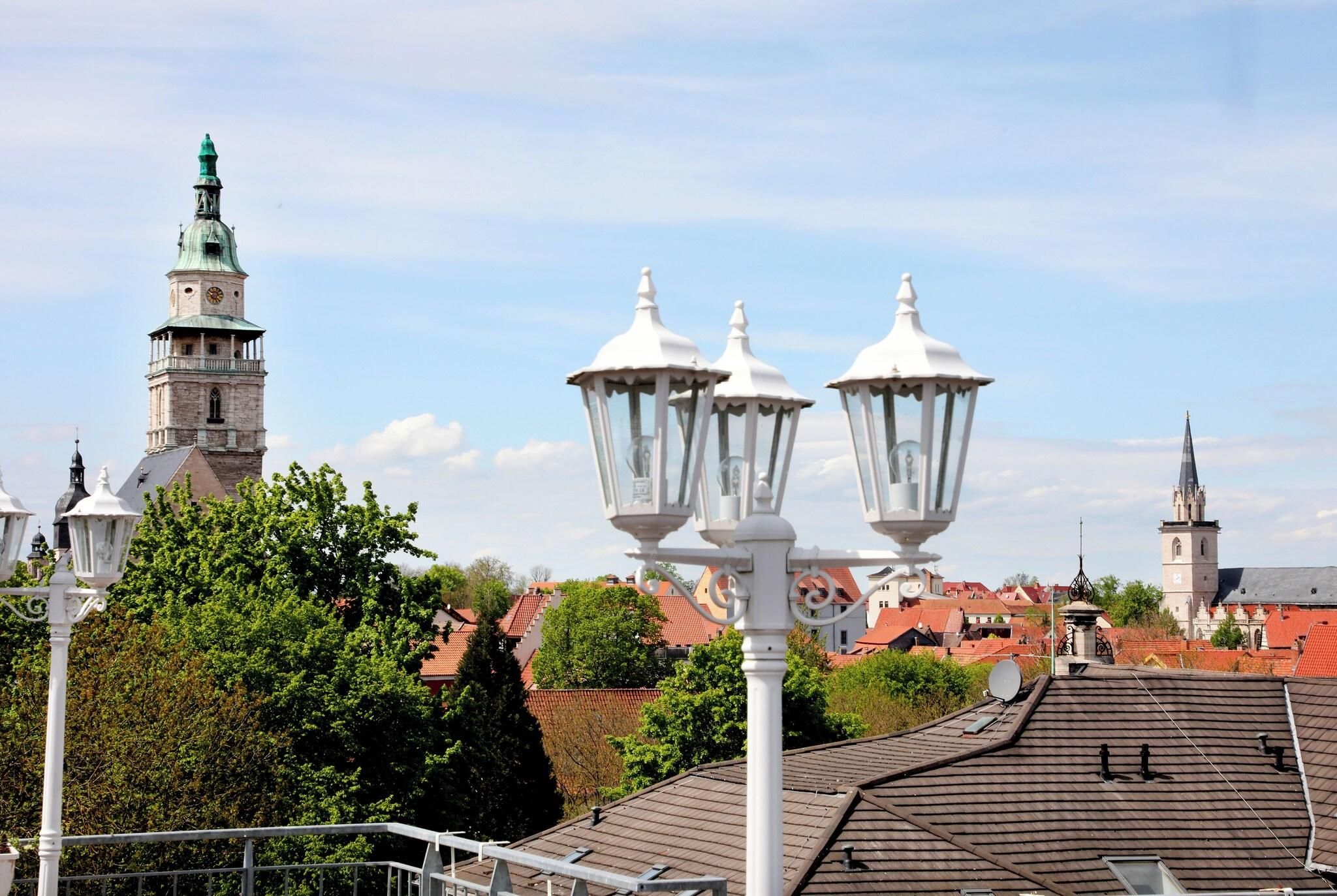 Blick auf eine Stadt mit einem markanten Turm, Straßenlaternen und Gebäuden mit roten Dächern.