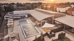 Un edificio moderno con piscina, mobiliario exterior y una amplia fachada de vidrio.