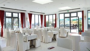 A dining area with tables set for service, large windows with red curtains, and a view of the outdoors. - Alpha (Bad Langensalza)