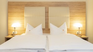A hotel room with a wooden headboard, two bedside tables with lamps, and a neatly made bed with white linens.