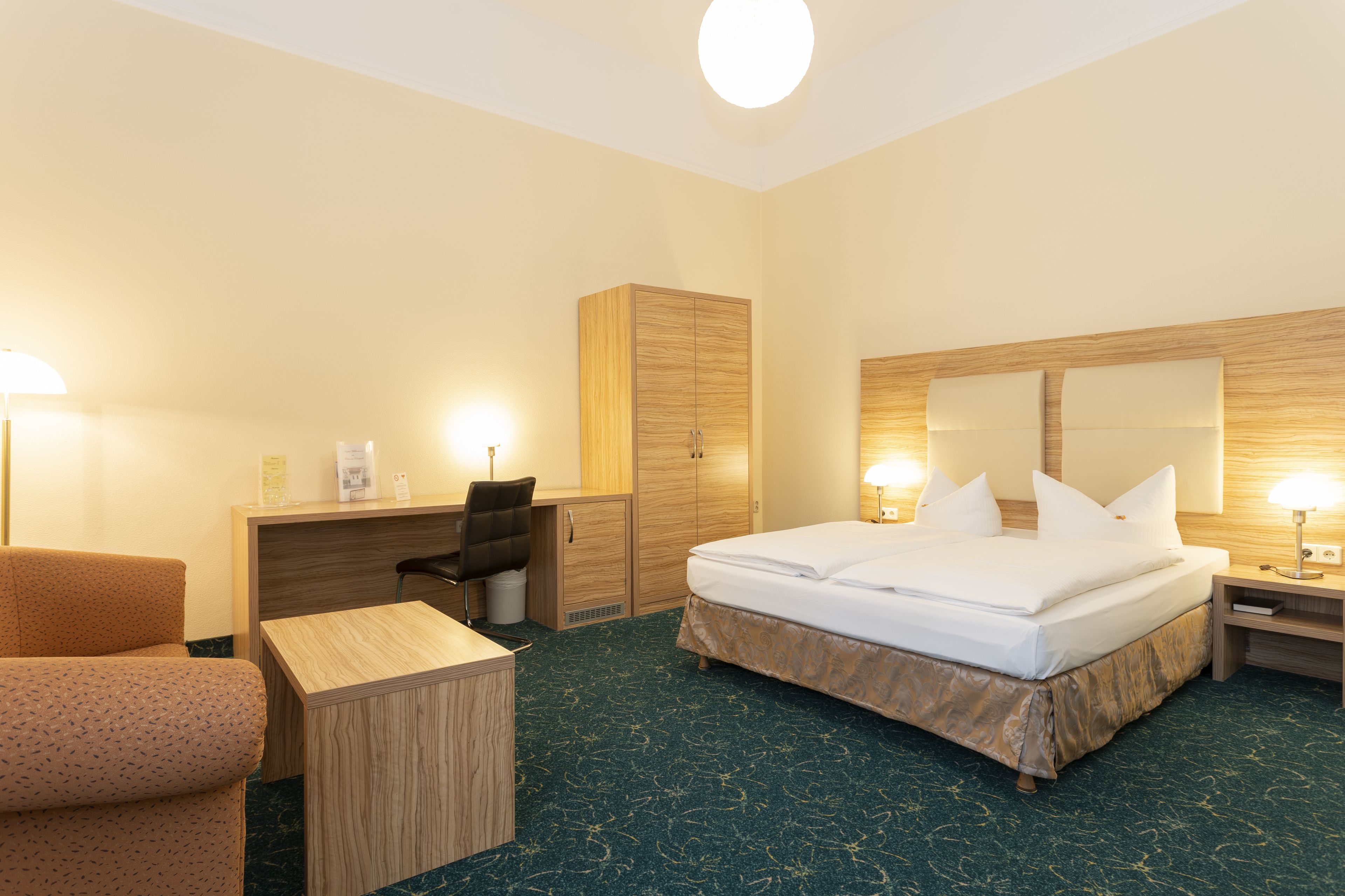 A hotel room with a bed, desk, chair, wardrobe, and bedside table.