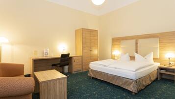 A hotel room with a bed, desk, chair, wardrobe, and bedside table.