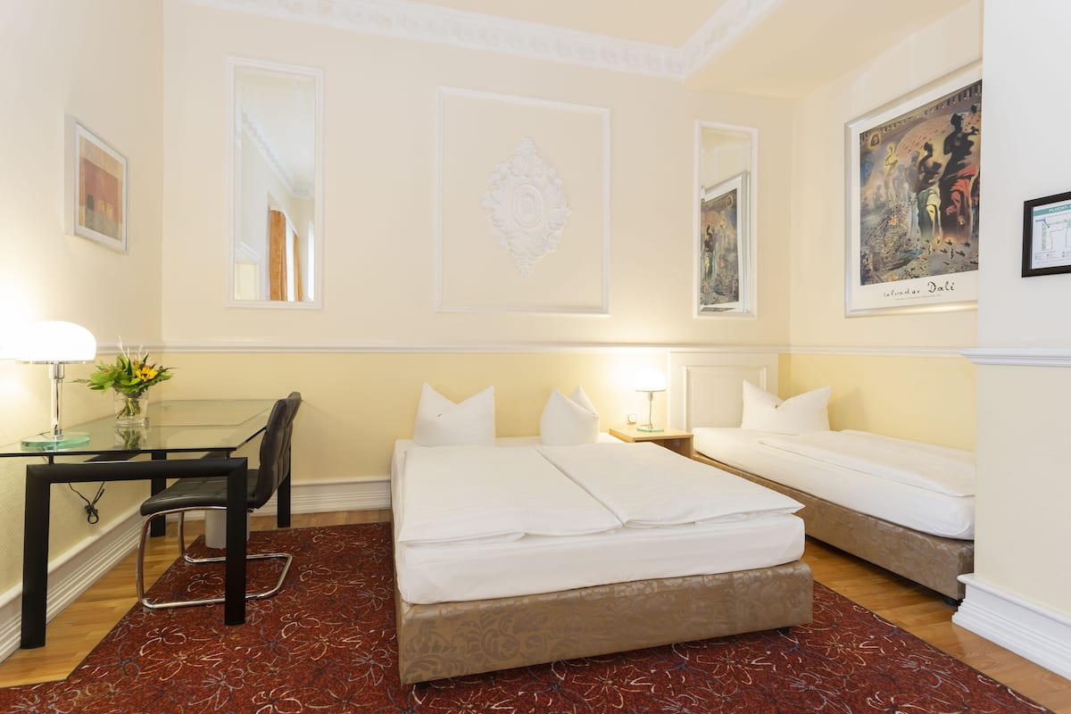 Habitación de hotel con escritorio de vidrio, dos camas, una silla y una alfombra roja estampada.