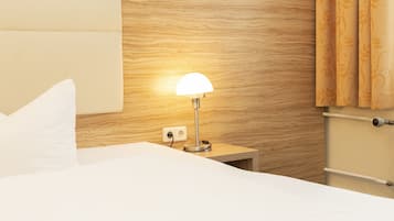 A neatly made bed with white linens, a wooden headboard, a bedside lamp, and a curtain with a floral pattern.