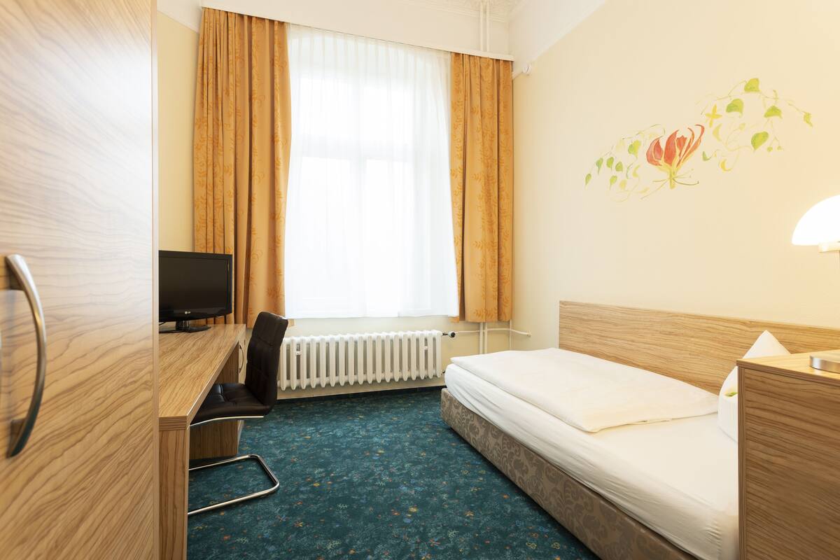 Una habitación de hotel con un escritorio de madera, una cama, un radiador y un televisor.