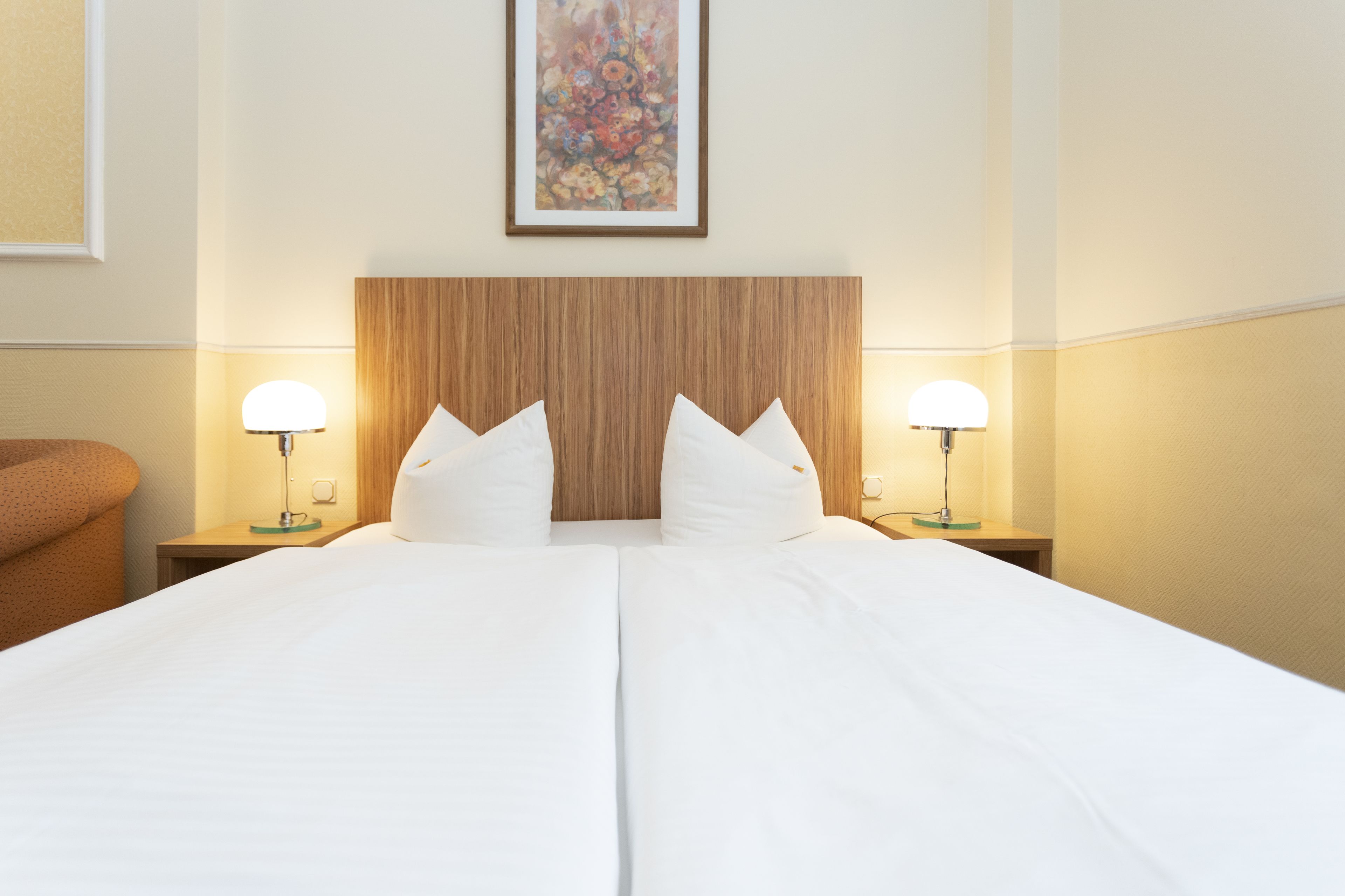 A hotel room with a large bed, two bedside lamps, a wooden headboard, and a framed floral artwork on the wall.
