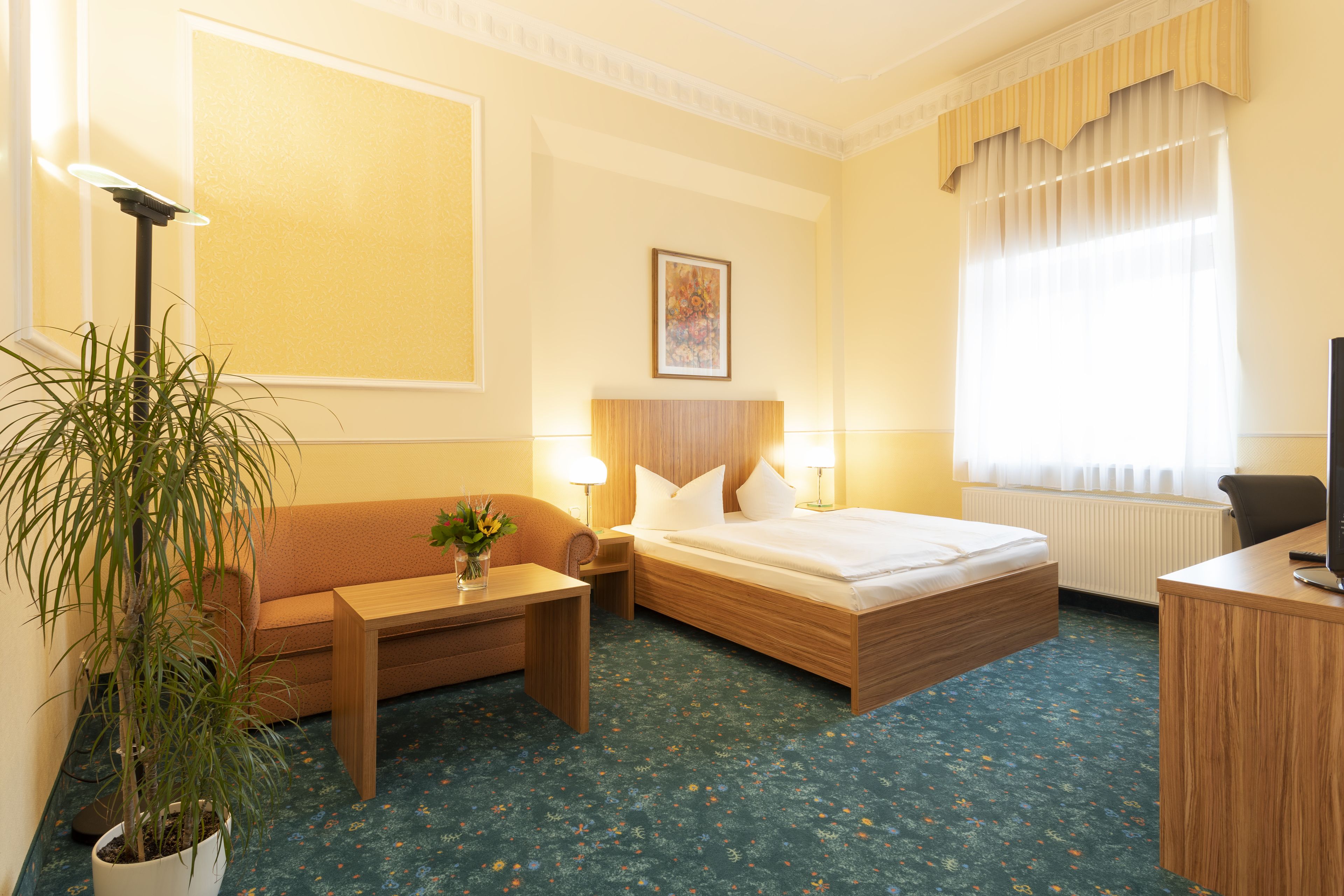 A hotel room with a bed, a sofa, a desk, a lamp, and a potted plant.