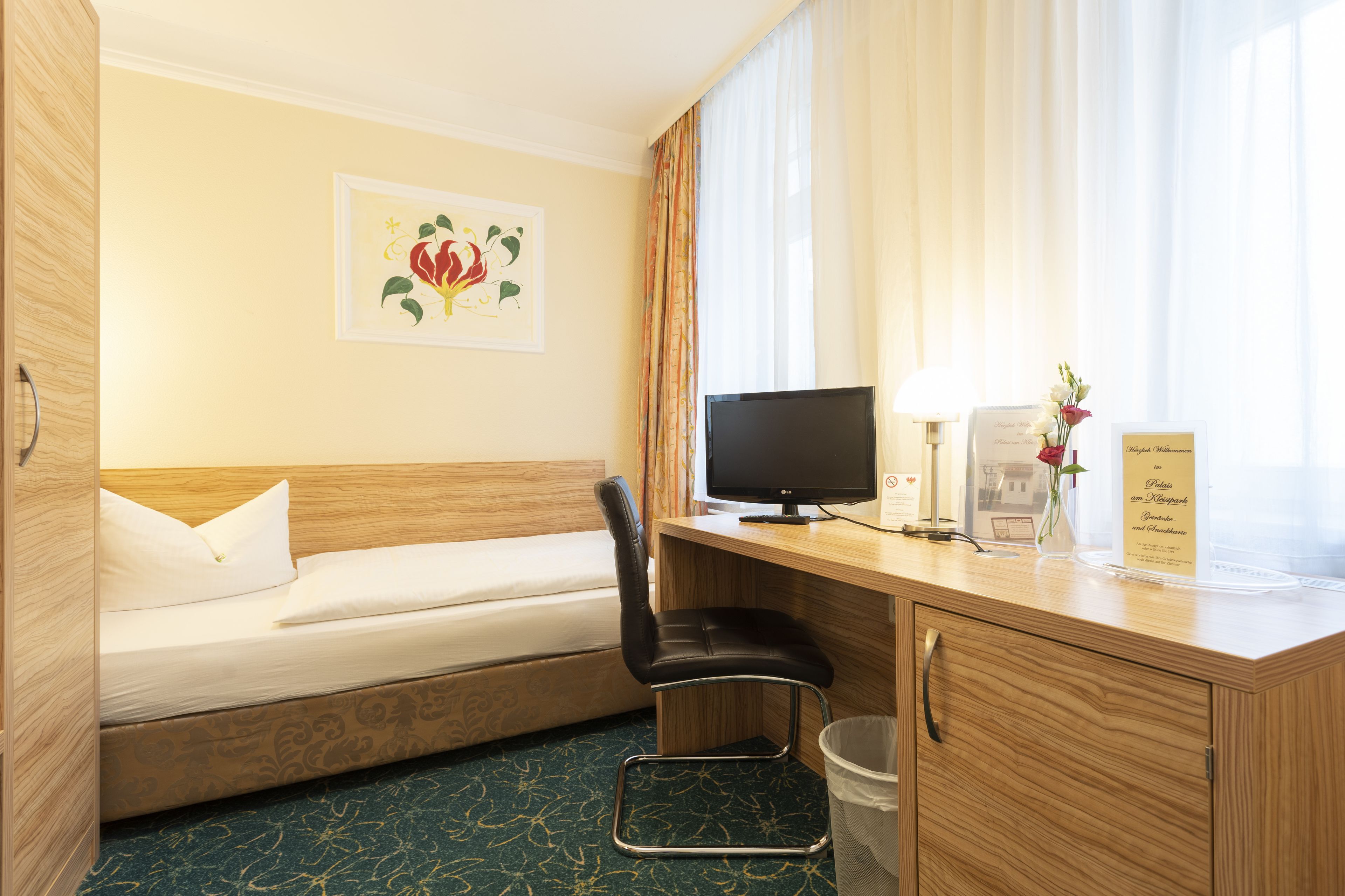 A hotel room with a bed, a desk with a computer, a chair, and a trash bin.