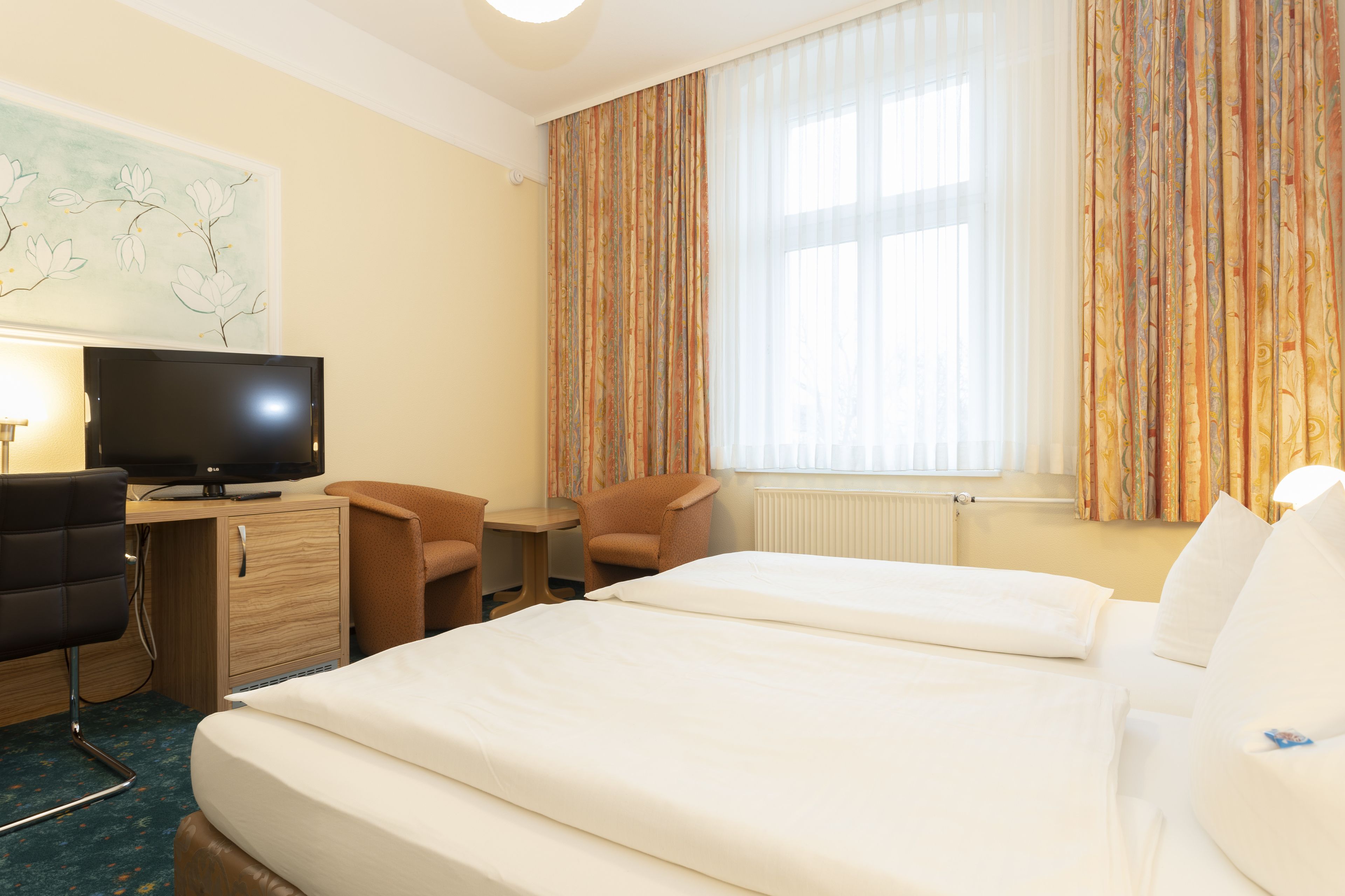 A hotel room with two beds, a desk with a television, a chair, and a window with curtains.