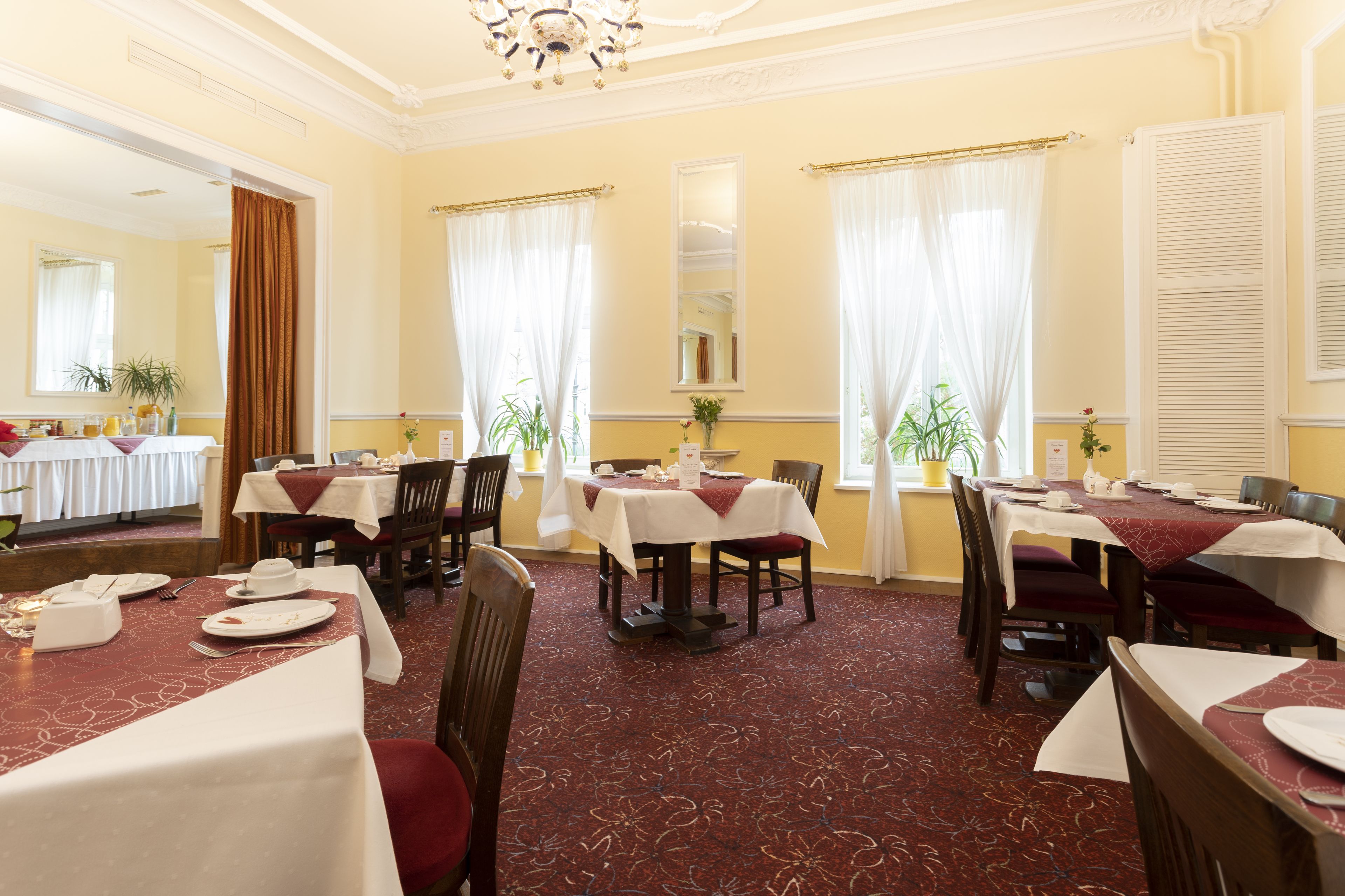 A dining area with multiple tables set for service, featuring a patterned carpet and classic decor.