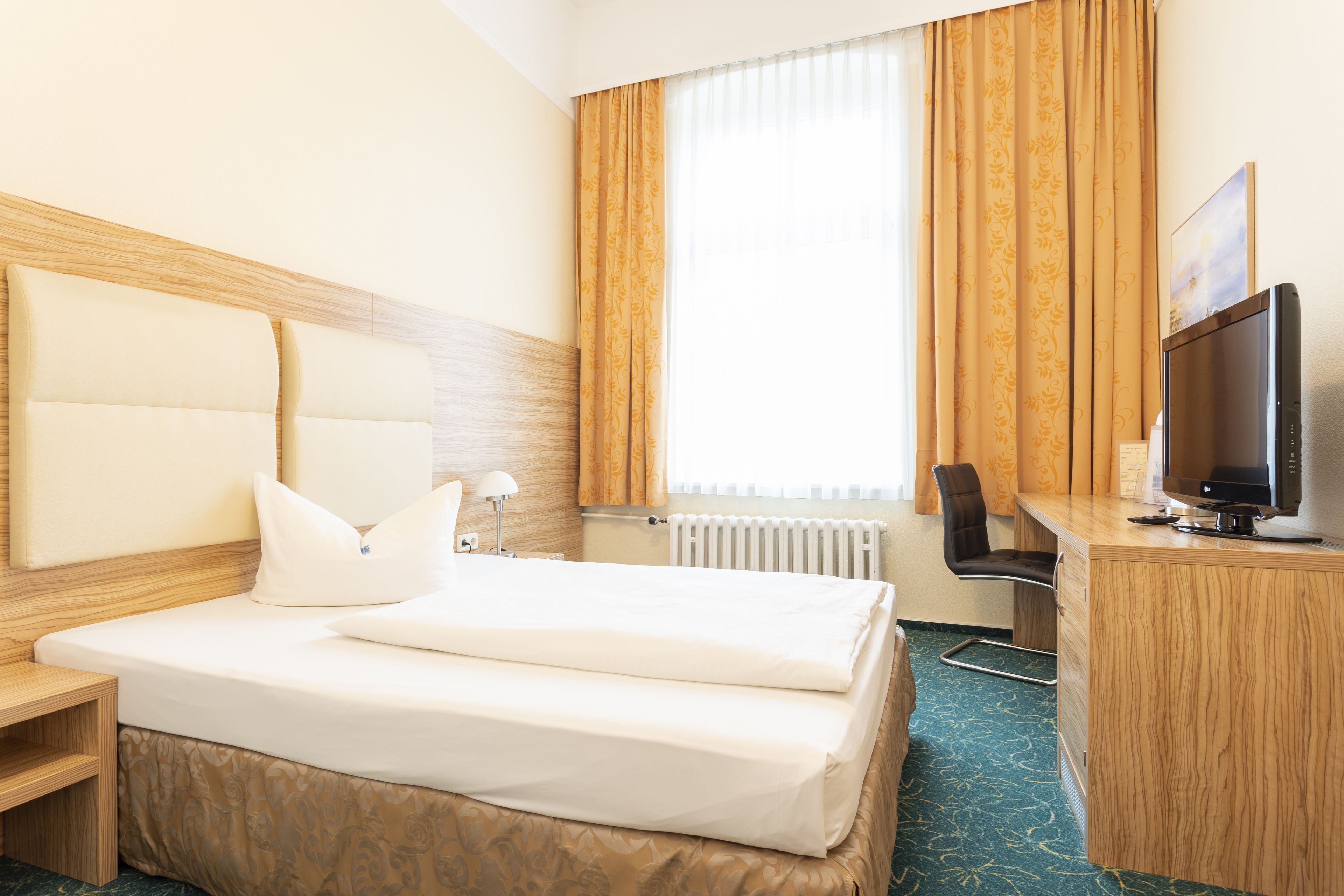 Una habitación de hotel con cama, escritorio, computadora, silla y televisor.