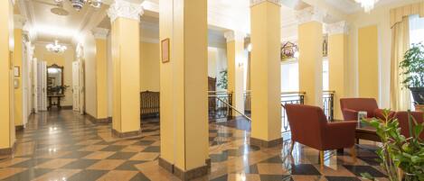 A hotel lobby with checkered flooring, columns, and a chandelier.