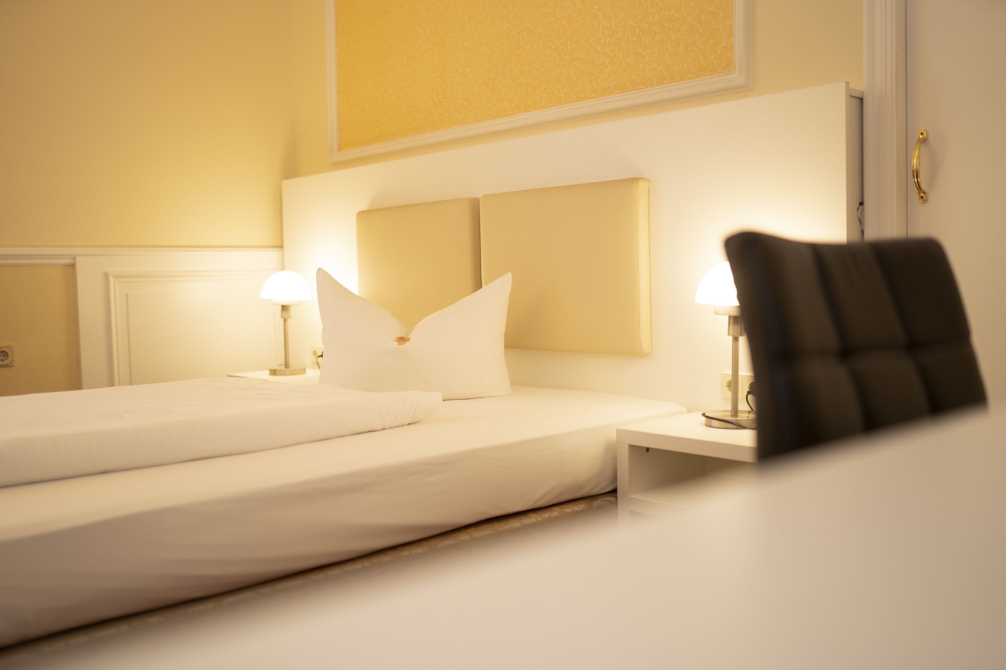 Una habitación de hotel con una cama bien hecha, dos lámparas de noche y una silla.