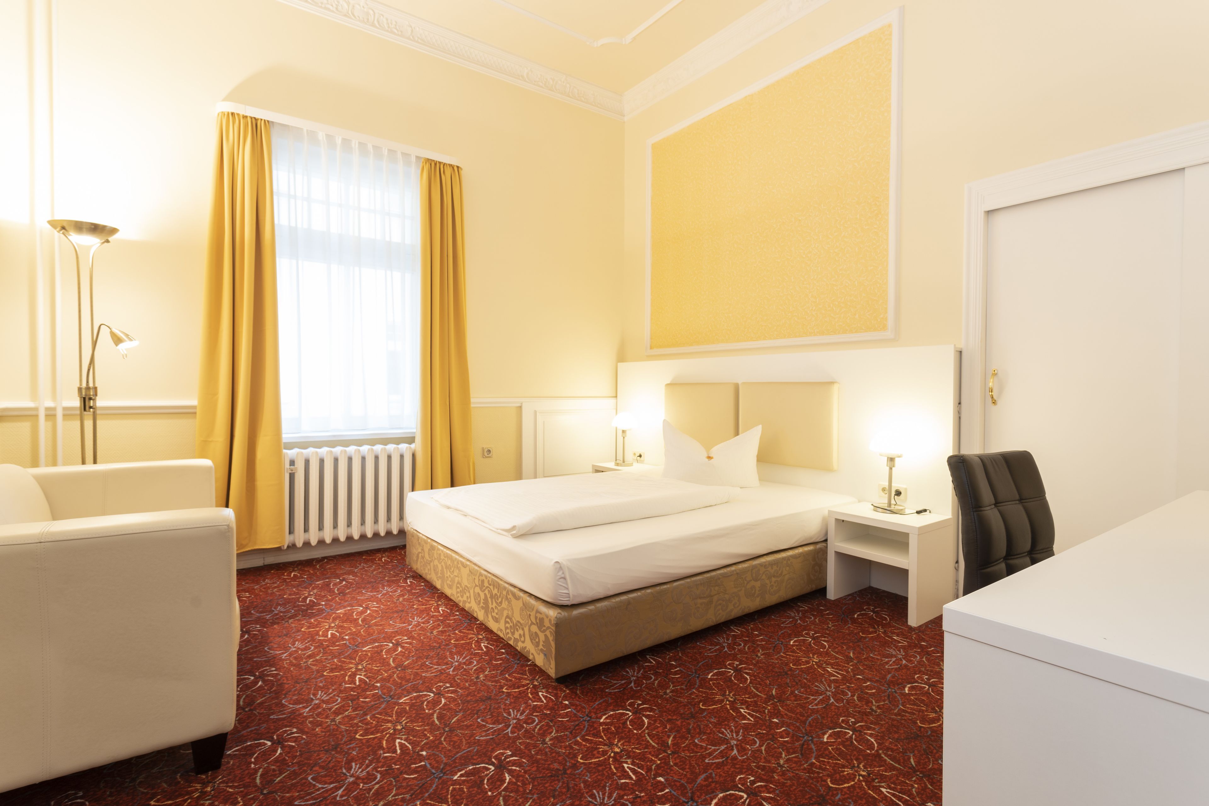 Een hotelkamer met een bed, een bureau, een stoel, een lamp en een radiator.