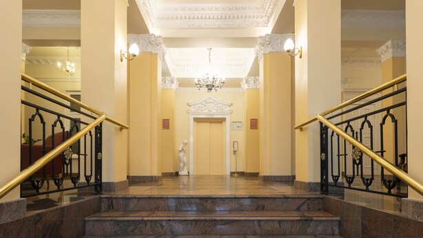 A grand staircase with marble steps and ornate black railings, leading to a door with a classical white design.