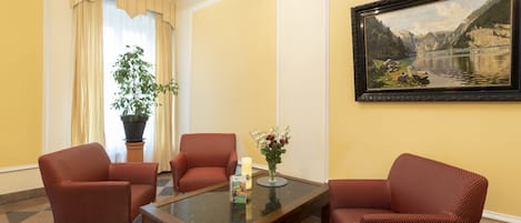 A hotel room with a large painting of a lake, a glass coffee table, and four red upholstered chairs.