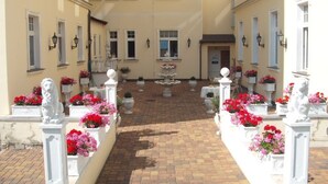A courtyard with a central fountain, surrounded by flower beds and white statues.