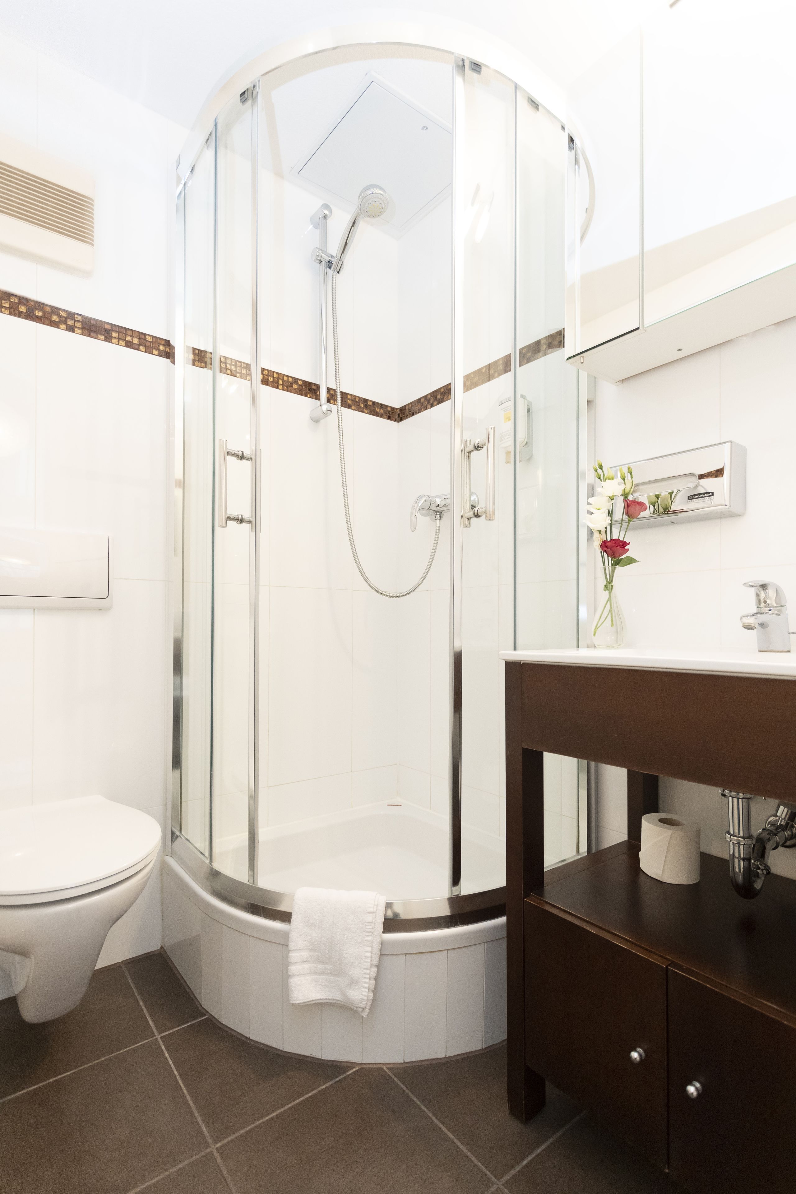 A modern bathroom with a glass-enclosed shower, a white toilet, and a dark wooden vanity.