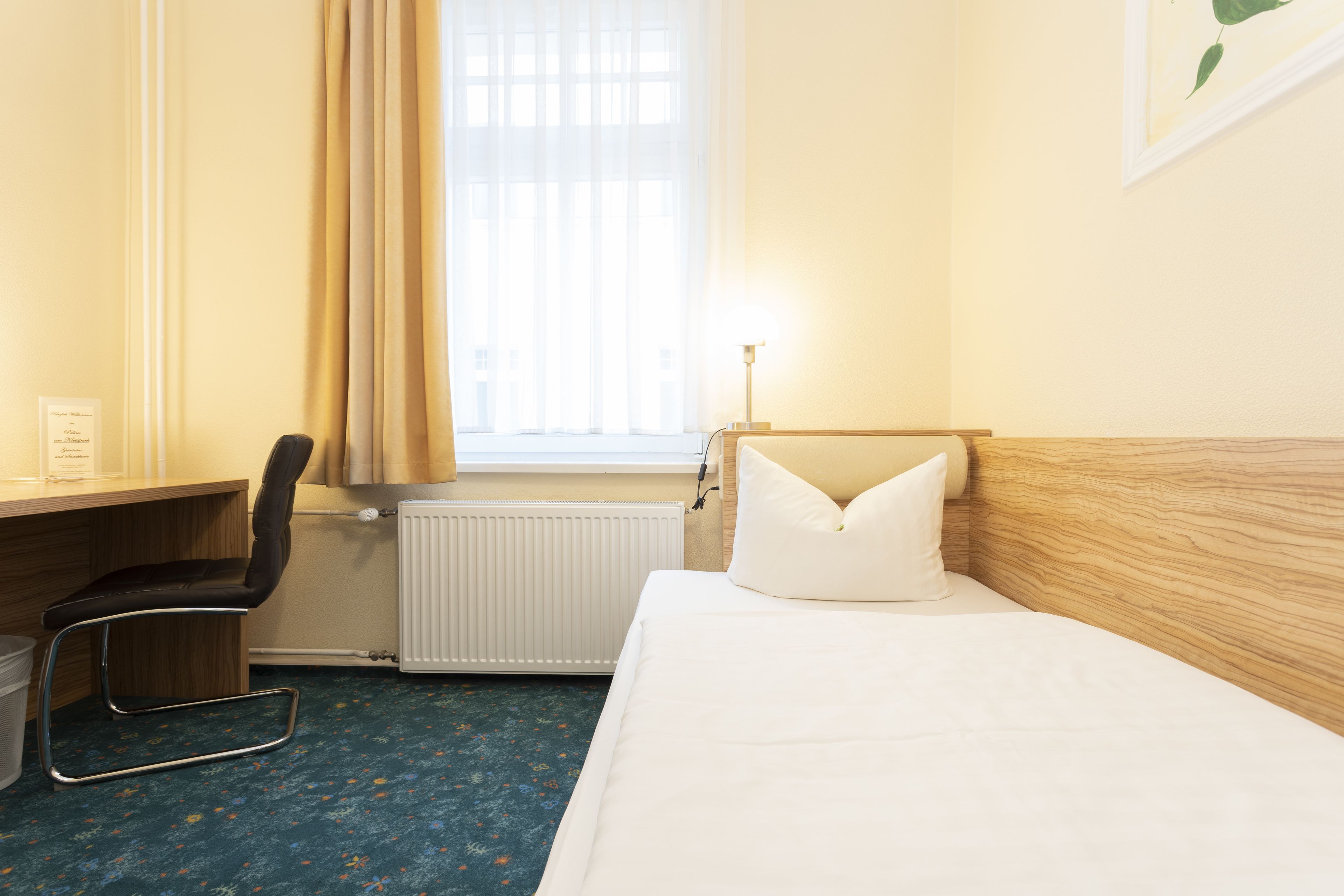 Ein Hotelzimmer mit einem Bett, einem Schreibtisch, einem Stuhl, einem Heizkörper und einem Fenster mit Vorhängen.