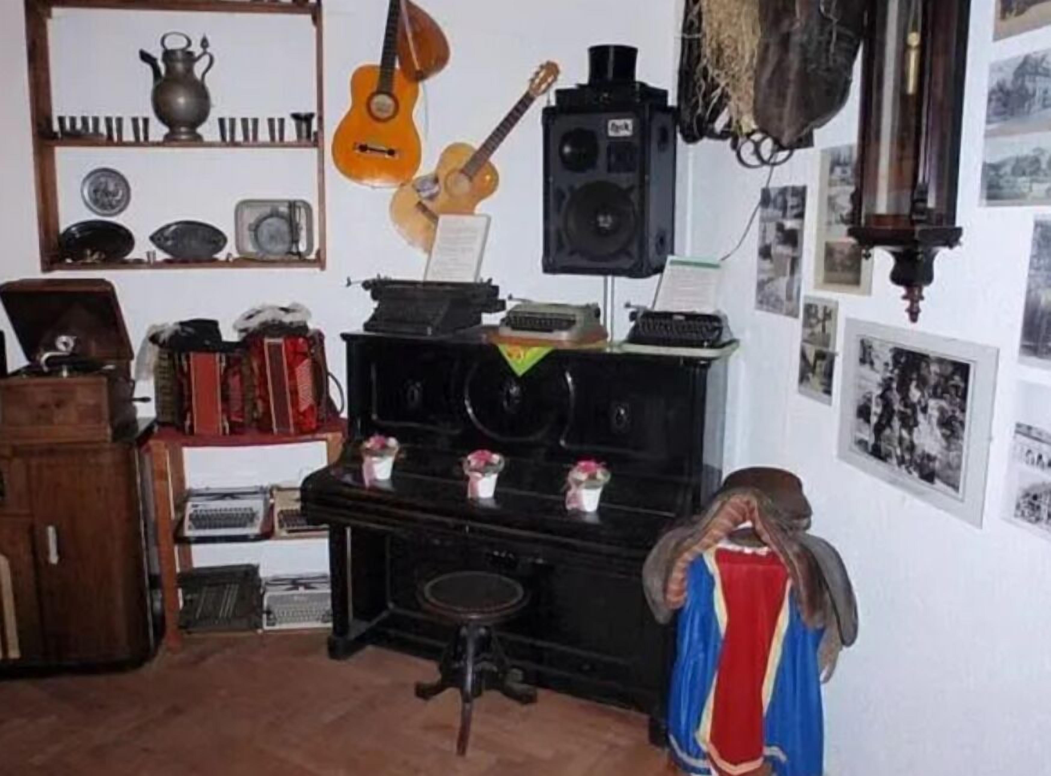 A room with a piano, a guitar, a speaker, and various items on shelves.