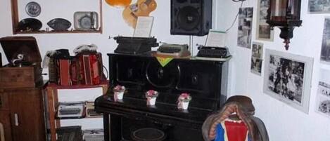 Una habitación con un piano, una guitarra, un altavoz y diversos objetos en estanterías.