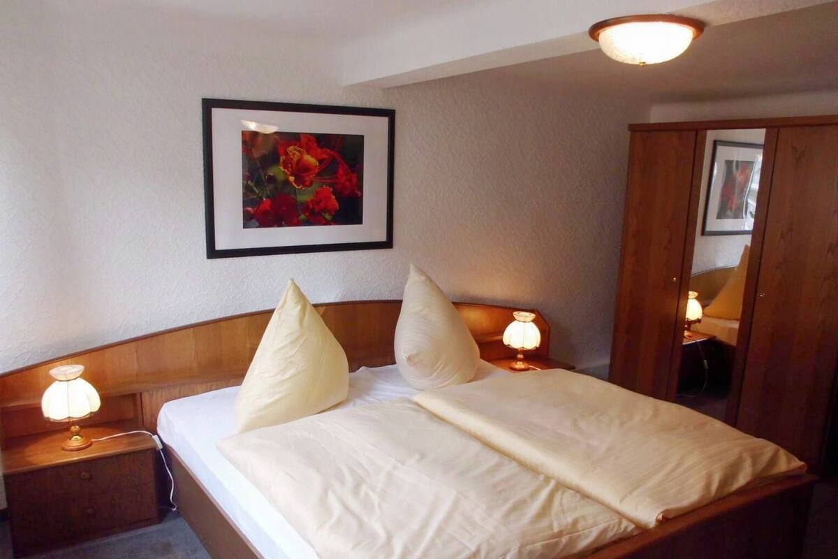 Une chambre d’hôtel avec un lit, deux lampes de chevet, un tableau encadré au mur et une armoire en bois.