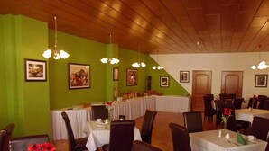 Un restaurant aux murs verts, doté de nombreuses tables et de lustres suspendus.