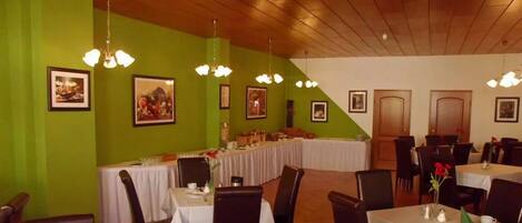 A restaurant with green walls, multiple dining tables, and hanging chandeliers.