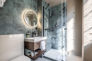 A modern bathroom with a glass-enclosed shower, a round mirror, and a white bathtub. - Hotel Jakob (Rapperswil-Jona)