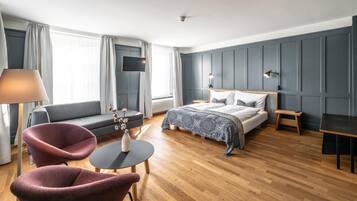 A hotel room with a bed, a sofa, a chair, a small table, and a desk.