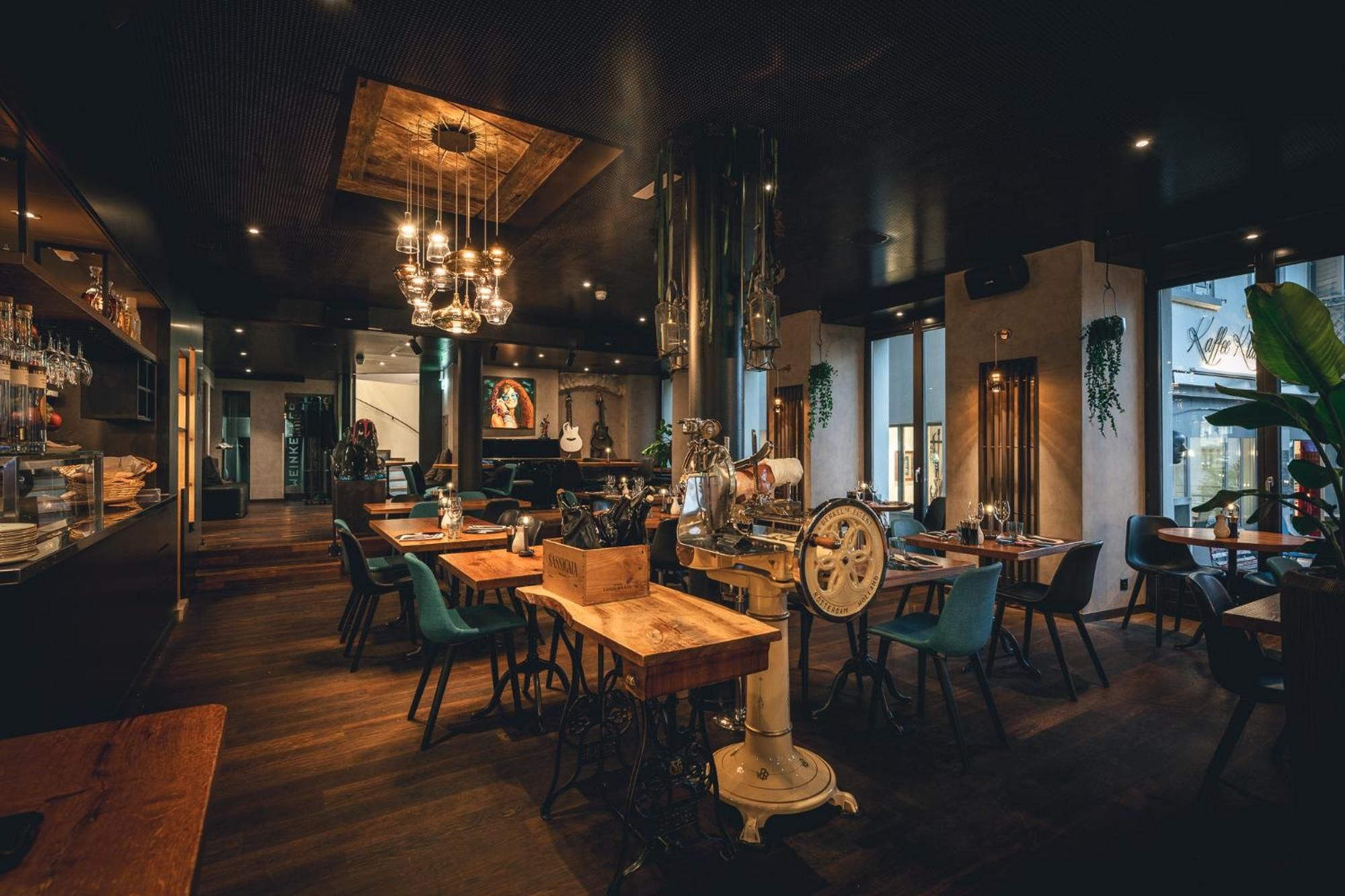 An interior with wooden tables, chairs, hanging lights, and a vintage espresso machine.